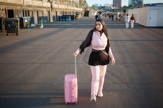 Woman in hijab walking with pink suitcase at sunset