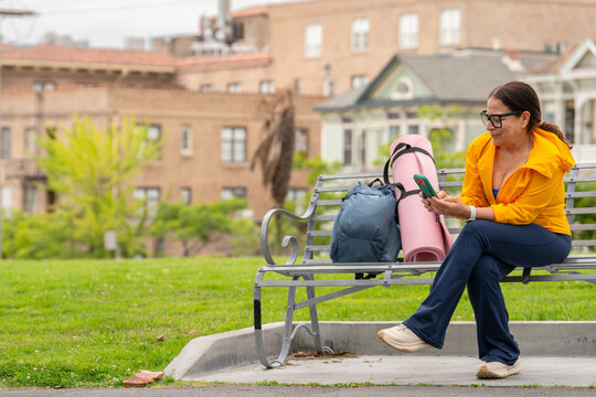 candid woman sitting on city park bench using smartphone
