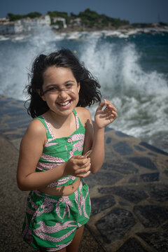 Little girl laughing as a wave crashes behind her in Cadaqu&eacute;s