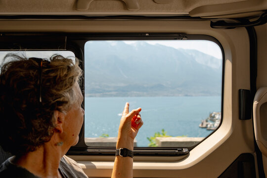 Senior traveler pointing at Lake Garda view from vehicle window