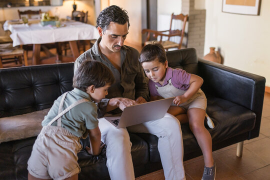 Father using laptop with his two young sons on sofa at home