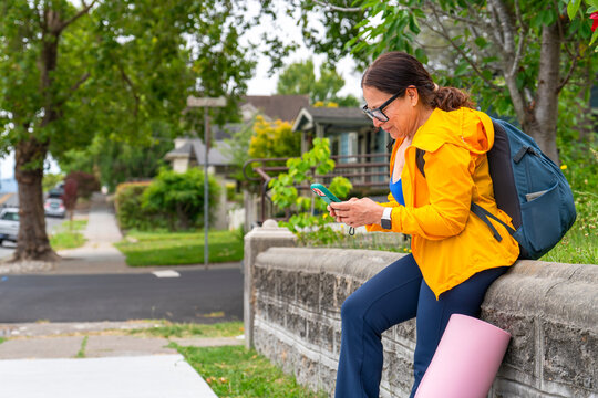 casual woman sitting by sidewalk using smartphone