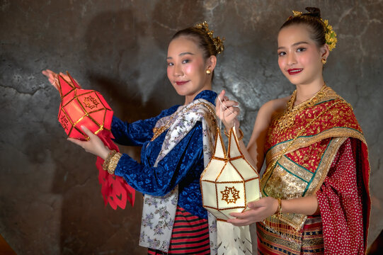 Two Thai women in colorful traditional Thai attires holding Lanna paper lantern celebrating Loy Kratong or Yi Peng festival in Chiang Mai