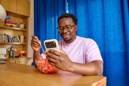 Man eating watermelon while checking his phone