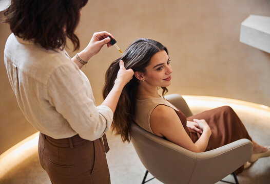 Stylist Applying Nourishing Hair Oil with Dropper to Client Scalp in Modern Salon with Warm Lighting