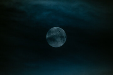 Bright full moon glowing in dark blue cloudy night sky. © Maria Sap