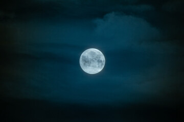 Bright full moon glowing in dark blue cloudy night sky. © Maria Sap