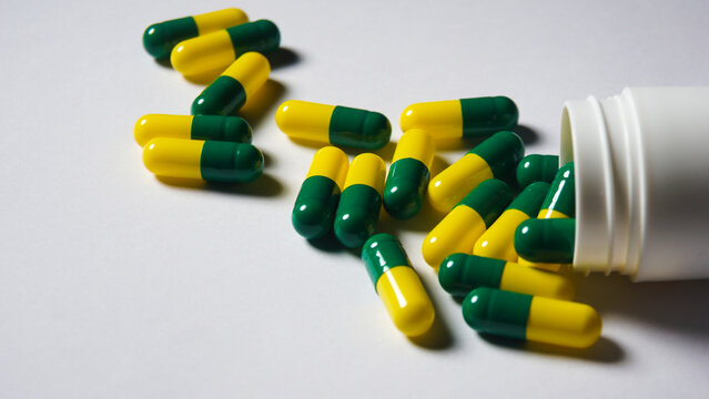 colorful capsules on white background. Green yellow capsules spilled from bottle. 