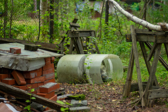 Birch log resting on wooden sawhorse in rustic country yard near bricks and plastic barrel.