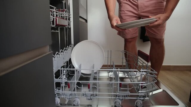 Man's hands carefully taking clean white plates out of the dishwasher after a wash cycle