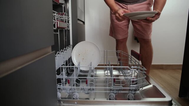 Man loading a dishwasher with dirty plates after a meal at home, helping with household chores
