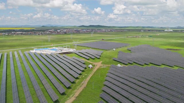 High-Angle Aerial View of Solar Power Station and High-Voltage Transmission Towers near Tangke Town in Zoige, Aba: Renewable Energy Base, Distant Town View, Green Prairie and Blue Sky Background