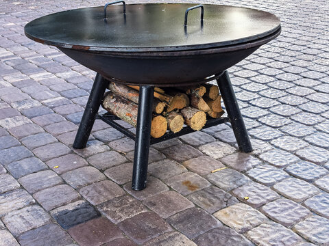 Black Metal Outdoor Fire Pit with Lid and Wood Storage on Stone Patio
