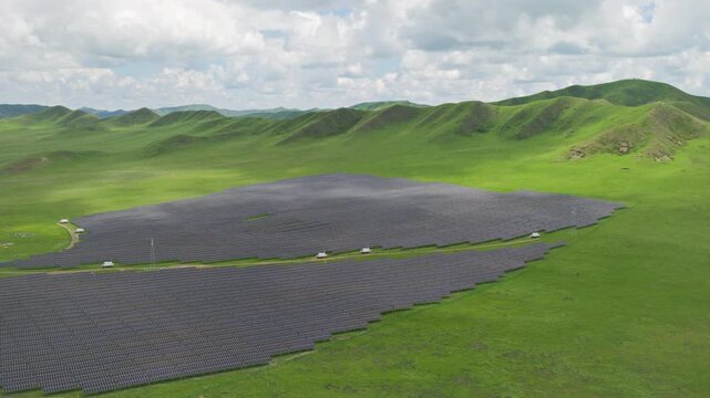 High-Angle Aerial View of Solar PV Panel Array on Zoige Grassland Mountains, Aba, Sichuan: Renewable Clean Energy, Agrivoltaics, Green Hills, Blue Sky and Cloud Background