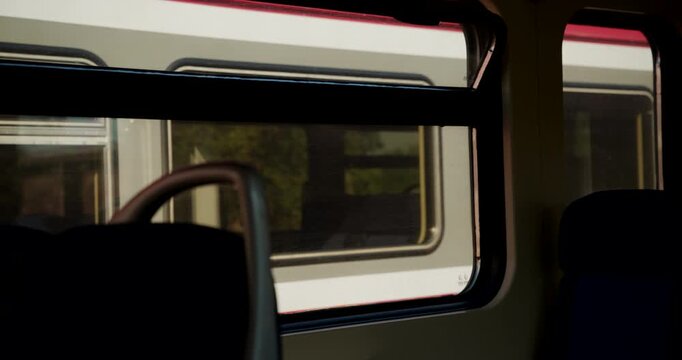 Silhouetted passenger walking through a stationary train seen through the window of an adjacent car. Concept of public transit, station stops, quiet travel moments, and passenger journeys. 4K.