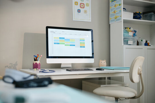 Computer displaying digital clinic appointment schedule on pediatrician workplace desk with stethoscope. Perfect for healthcare management software and medical advertising