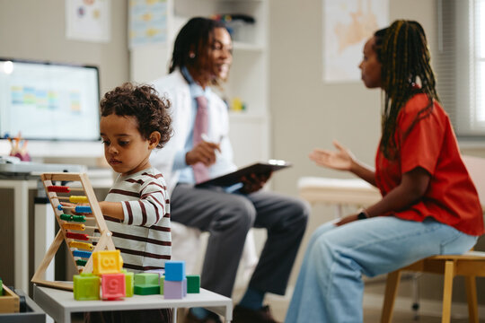 African American child playing with abacus while Black pediatrician consulting mother in medical office. Useful for pediatric healthcare, family wellness, child development campaigns