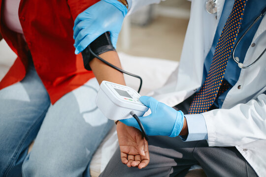 Male pediatrician measuring blood pressure of African American teenager using digital monitor during medical checkup. Image suitable for pediatric healthcare campaigns