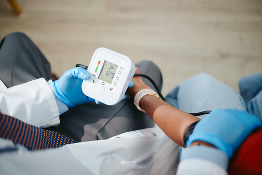 Top view of Caucasian doctor measuring blood pressure of Black teenage girl patient using digital tonometer. Concept of pediatric examination, useful for healthcare and medical clinic advertising