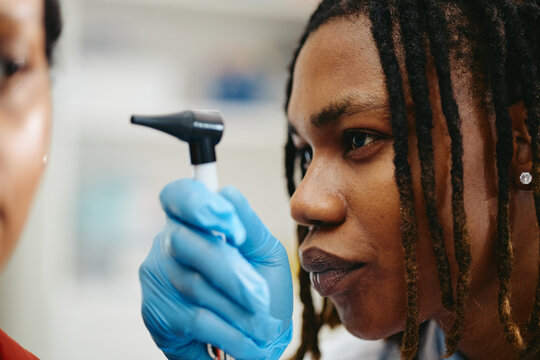 Close up of African American young adult pediatrician examining ear with otoscope during medical checkup. Concept represents pediatric healthcare, suitable for clinic advertising