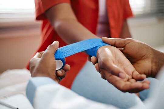 Close up shot of African American doctor applying bandage on wrist of young adult woman patient in clinic. Healthcare image suitable for first aid, emergency medicine or insurance