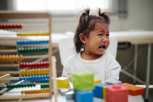 Asian toddler crying during pediatrician appointment in clinic office with colorful educational toys. Image useful for pediatric healthcare campaigns and child wellness promotion