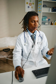 Vertical shot of African American young adult male pediatrician wearing headset and consulting patients online. Image suitable for telemedicine marketing