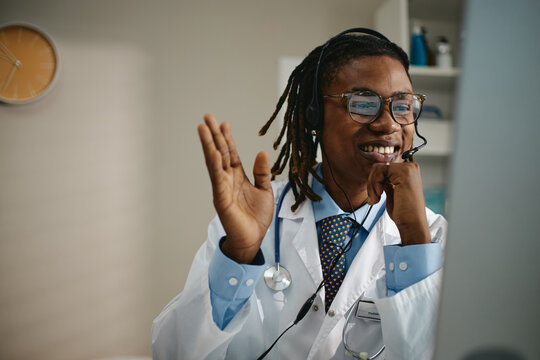 Smiling African American male pediatrician wearing headset waving during online consultation on computer. Visual concept for telehealth services and digital medical care advertising
