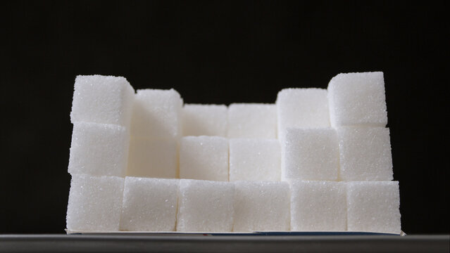 White sugar cubes stacked in a rectangular formation with a hollow center against a black background.