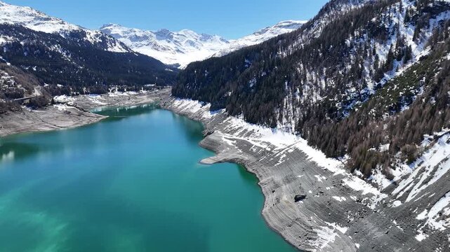 glaciated peaks tower over lai da marmorera reservoir turquoise water stretches valley drawdown shoreline rings banks forested slopes rise toward julier pass drone footage graubunden switzerland