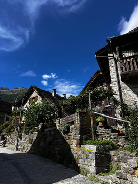 Traditional swiss alpine village with rustic stone houses, wooden balconies, mountain scenery and deep blue sky with wispy clouds