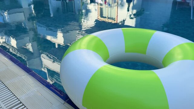 Colorful inflatable pool float with green and white stripes rests beside a clear swimming pool, reflecting sunlight and surrounding structures in a family-friendly vacation setting