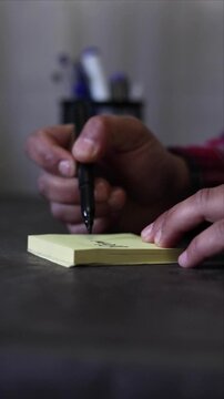 A vertical view of a person's hands writing the word &ldquo;Optimize&rdquo; on a sticky note on an office desk