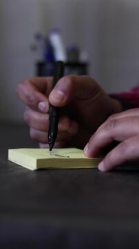 A vertical view of a person's hands writing the word &ldquo;Efficiency&rdquo; on a sticky note on an office desk