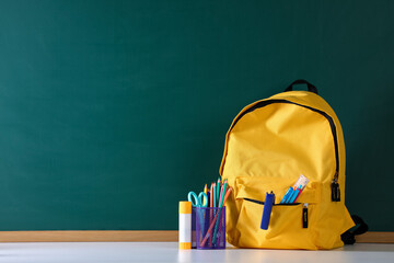 Backpack with stationery on white desk against chalkboard. Space for text © New Africa