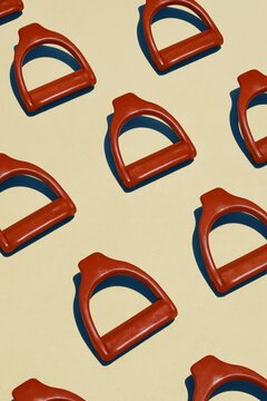 Horse riding stirrup irons in caramel brown arranged in a repetitive pattern on a luminous off-white background for equestrian design and decor