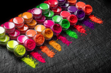 Obraz premium Colorful powdered pigments arranged on a black background with jars and lines of color. Colorful jars of powdered pigments sit side by side on a black surface with lines of color.