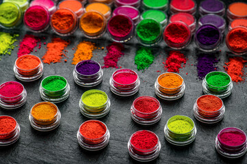 Obraz premium Bright colors of powdered pigments displayed in small jars on a dark surface. Various jars filled with bright powdered pigments are arranged on a dark table surface.