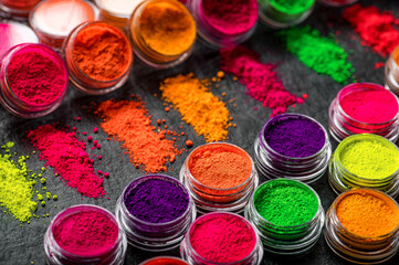 Obraz premium Colorful powders arranged in small containers on a flat surface. Bright colored powders are placed in containers on a dark surface.