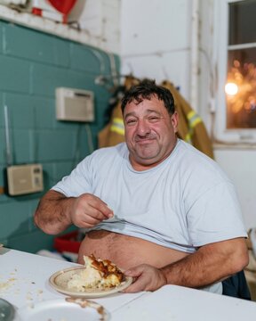 Slice of cake on a plate being eaten by a smiling firefighter in a station kitchen, natural moment for fire services and food brands