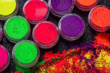 Obraz premium Bright colored powders laid out on a dark surface for creative uses. Jars of colored powders in shades of green, pink, purple, and orange are arranged on a surface.