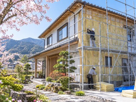 Trabajadores en una casa durante la construcci&oacute;n en un paisaje de primavera con flores de cerezo en el fondo