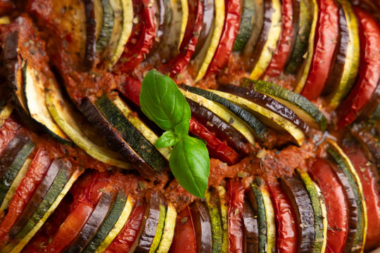 Vegetable ratatouille dish with layers of tomatoes zucchini and eggplant topped with fresh basil in a baking dish