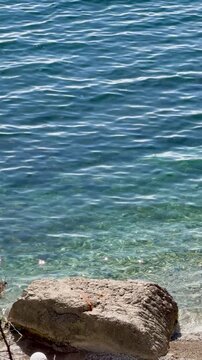  Clear seawater and large rock at shoreline with gentle ripples, vertical