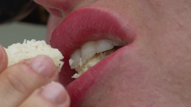 Confectionery dessert tasting by woman taking bite of white coconut candy in extreme macro closeup shot.