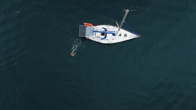 Aerial view of the sailing boat in the calm sea. Man jumps from the boat and swims in the water nearby