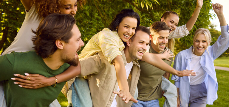Friends group cheering smiling together in diverse park. Happy youth enjoy fun piggyback rides. Candid moment in green park shows connection and positive energy. Concept of friendship and joy.