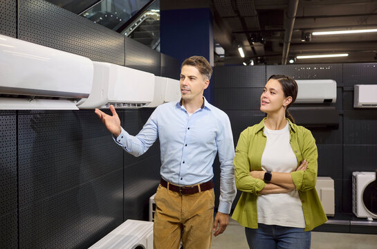 Couple customers shopping appliances in retail store. They are choosing a wallmounted unit while smiling. Consumer buying decision in a showroom. Clear consumer purchase decision concept.