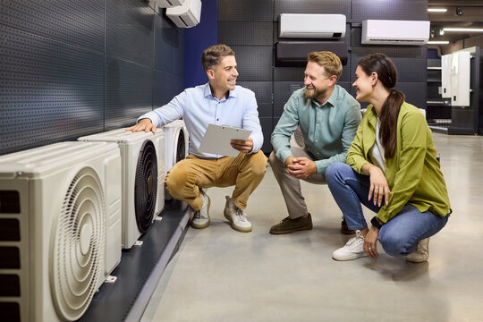 Salesman advises couple choosing airconditioner in store. They review units, efficiency, pricing, warranty and installation options. Retail consultation advice and purchase decision concept.