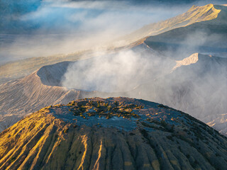 Aerial view of Gunung Batok rugged volcanic slopes, crater terrain, drifting mist, and sunlit mountain ridges in Indonesia. © Cloudyew